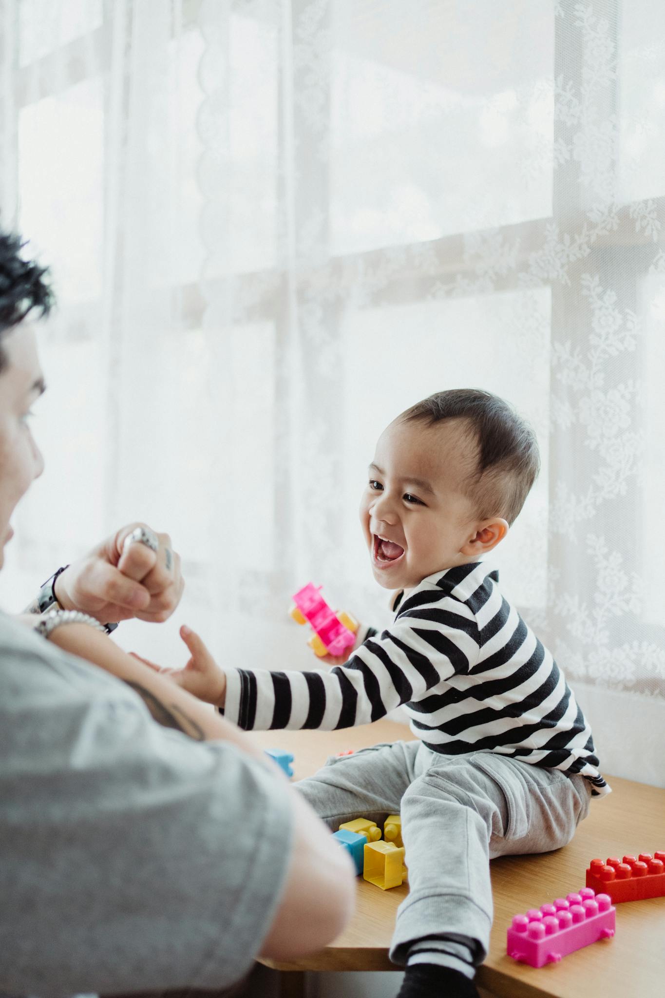 A joyful moment of bonding between a father and child playing with building blocks by the window.